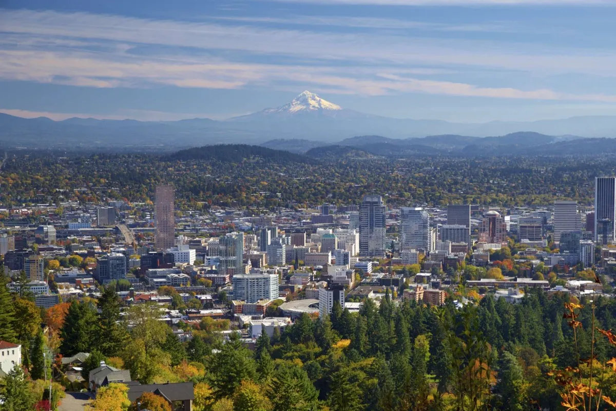 A sweeping view of downtown Portland with Mount Hood and green hills in the background, capturing the broader context of the region and its possibilities for exploration and outdoor activities.