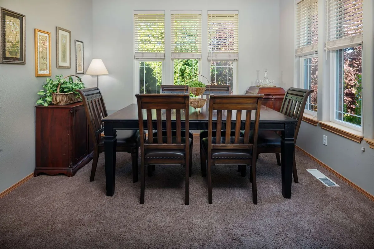 A dining table surrounded by wooden chairs sits next to a window, letting in natural light and offering a view of the outdoors. The table is set for a group, and small decorative touches like a plant and side cabinet make the area feel warm and inviting—perfect for meals, gatherings, or even remote work.