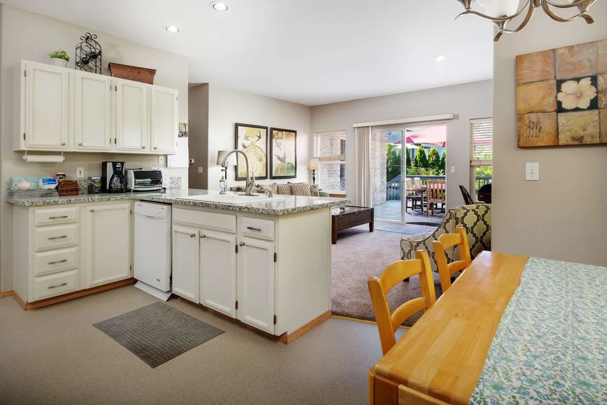 This image features an open-plan layout with a kitchen island, a spacious dining table, and views leading out to an outdoor patio. The scene conveys a lively, cohesive space where cooking, dining, and relaxation all flow together seamlessly. There are multiple seats at the dining table, plenty of prep space, and natural light streaming in from the patio doors.