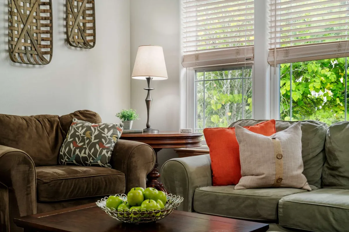 A warm, welcoming interior space with green apples in a bowl, decorative pillows, and natural light streaming through the blinds. The setup hints at relaxing with a drink and enjoying the view from a cozy spot inside the retreat.